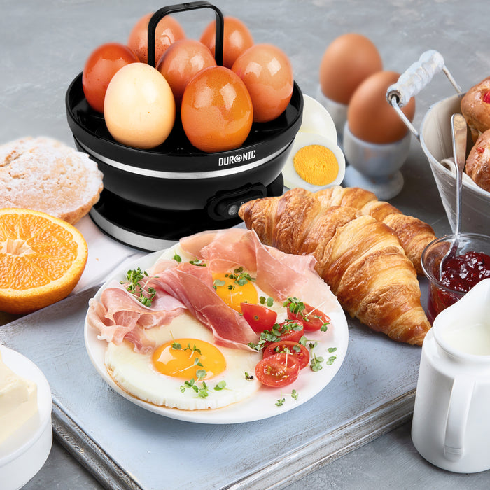 Duronic EB27 BK electric egg boiler cooking 7 eggs surrounded by delicious food like croissanta