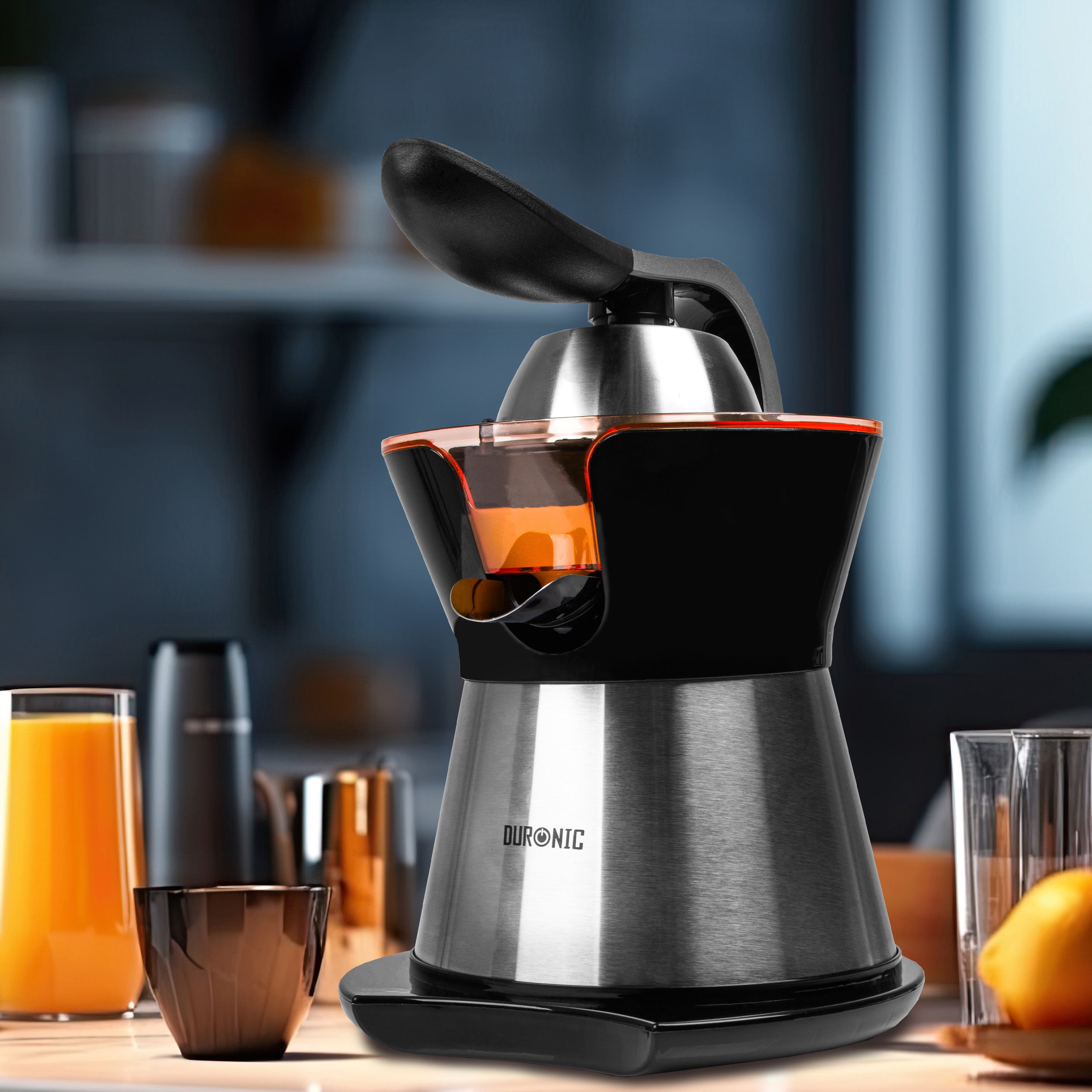 Duronic Electric Citrus Juice with a black lever handle and spout sits on a kitchen counter next to a glass of fresh orange juice.