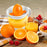 Duronic Electric Citrus Juicer with orange and white manual citrus juicer sits on a wooden table alongside fresh orange halves, raspberries, a glass of juice, and a bowl of cereal.