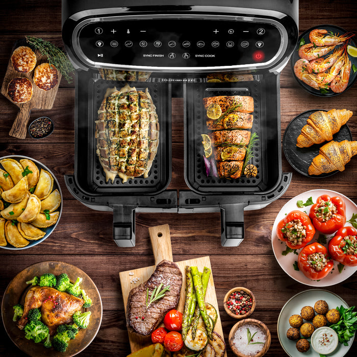 Duronic Twin Drawers AFD2 BK view of a dual-basket digital air fryer surrounded by various cooked dishes like steak, salmon, stuffed peppers, and croissants