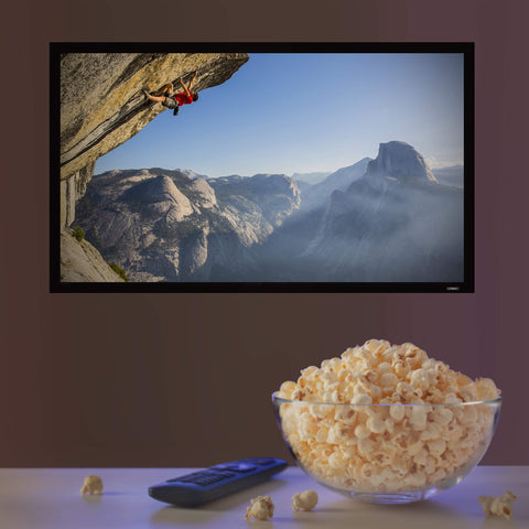 A large bowl of popcorn and a remote control sitting in front of a wall-mounted TV screen.