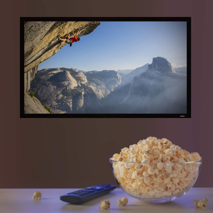 A large bowl of popcorn and a remote control sitting in front of a wall-mounted TV screen.