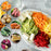 A vibrant assortment of spiralized vegetable noodles including zucchini, carrot, and beet served on a white platter with cubed tofu and circular insets showcasing the fresh whole vegetables.