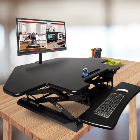 Duronic DM05D5 Corner Sit-Stand  Desk with a monitor mount, keyboard tray, and built-in tablet slot sitting on a wooden desk.