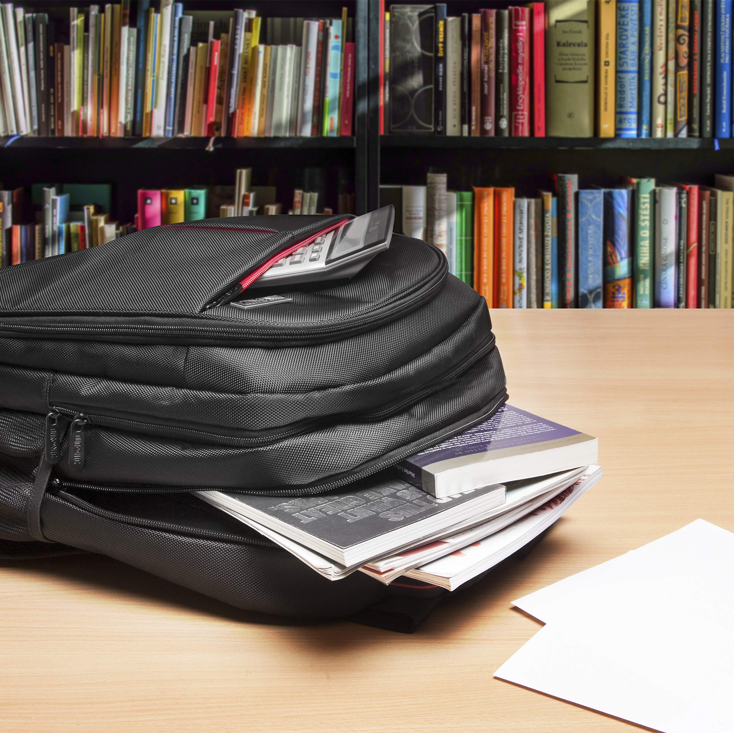 Duronic Laptop Backpack stuffed with books and a calculator on a table before a bookshelf.