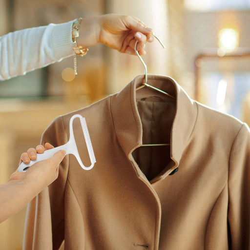 Duronic Lint Shaver being used to clean a tan wool coat on a hanger.