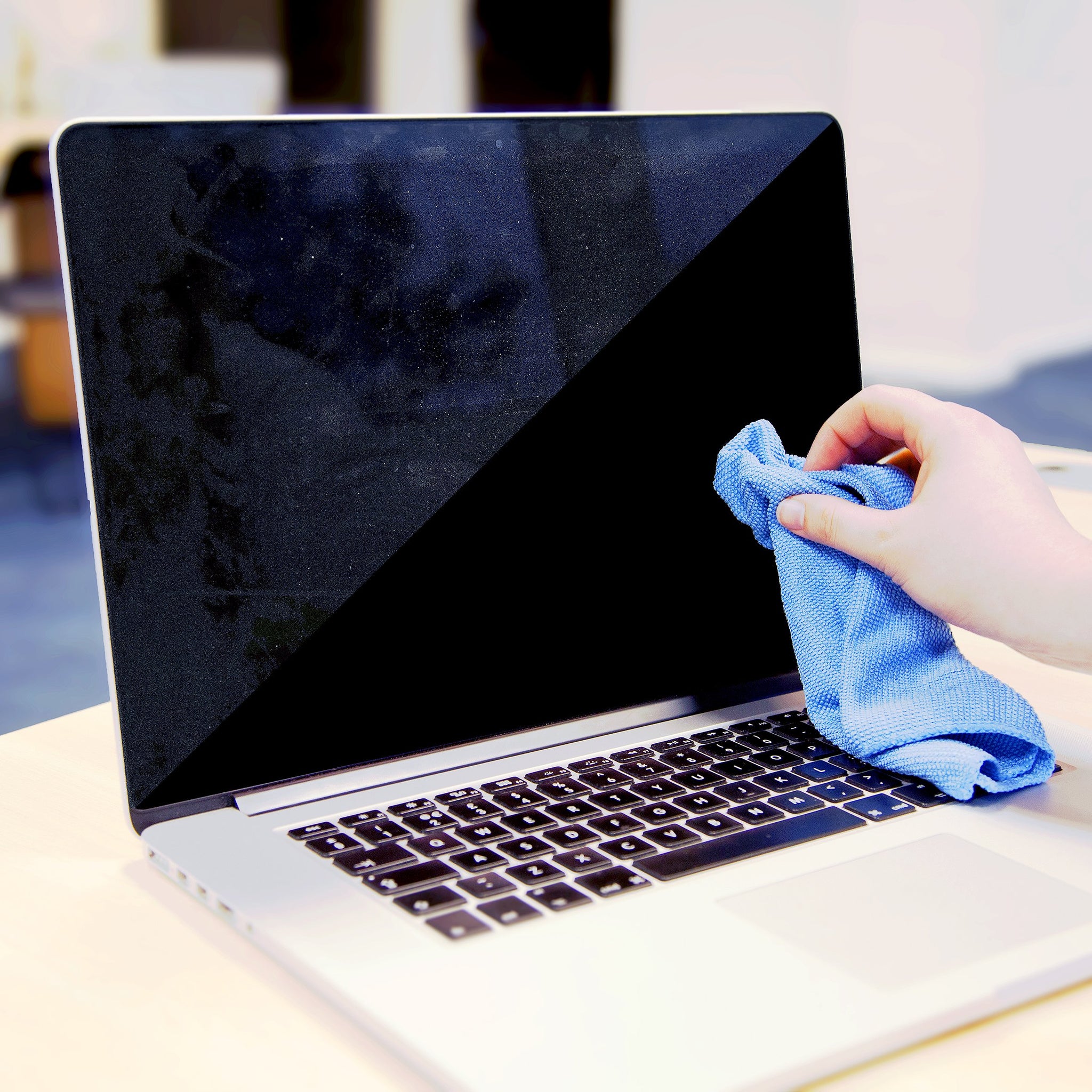 Duronic Screen Cleaner with a Hand wiping a dirty laptop screen with a blue microfiber cloth on a desk.