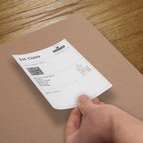 Duronic Thermal Labels close-up shot of a hand peeling a Royal Mail 1st Class shipping label onto a brown cardboard package.