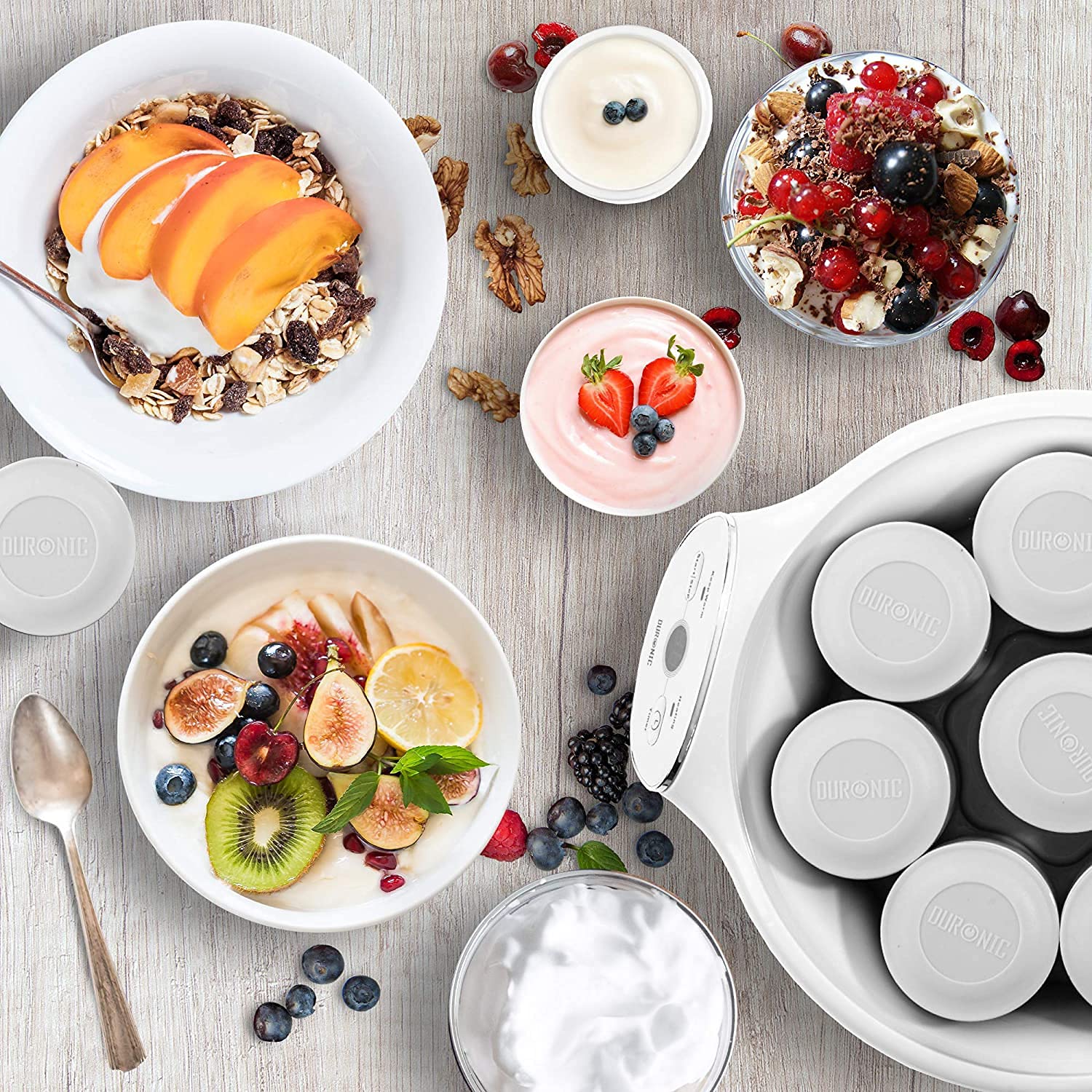 Duronic yogurt maker machine surrounded by fruit, muesli, and bowls filled with fresh homemade yogurt.