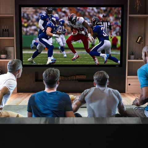Four men watching an American football game on a large home theater projector screen.